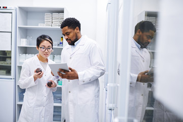 Content experienced multi-ethnic pharmaceutical workers in lab coats standing in storage room with...