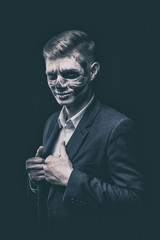 Stylish and beautiful, emotional young man with skeleton makeup in a strict suit against the background of smoke and dark background to Halloween