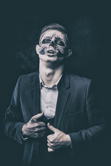 Stylish and beautiful, emotional young man with skeleton makeup in a strict suit against the background of smoke and dark background to Halloween