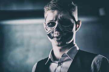Stylish and beautiful, emotional young man with skeleton makeup in a strict suit against the background of smoke and dark background to Halloween