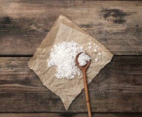 large white salt on a brown piece of paper and a wooden spoon