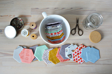 Hexagon english paper piecing templates, white cup, thread, retro scissors, metal pins and glass jar on the wooden table