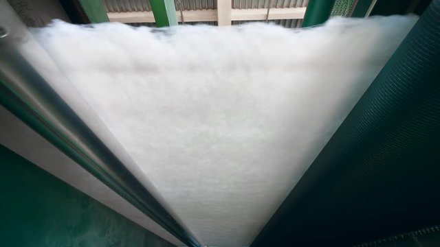 Factory rollers press white polyester batting into a thin layer.