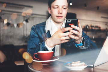 Man with mobile phone in hands, laptop and cup of coffee working in city cafe. Smart casual dress