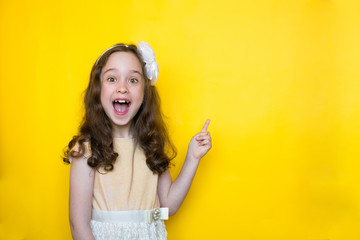 smiling little girl on yellow background points her finger at the space for lettering. Concept of...