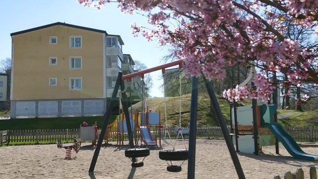 Slow tilt down shot of an empty playground in Uddevalla, Sweden, with a beautiful pink Magnolia tree in the foreground
