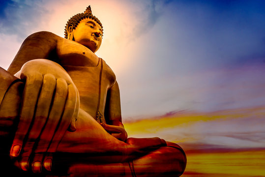 The large golden lord of Buddha statue that is faithful on a beautiful and colourful sky with orange, yellow, red, blue.