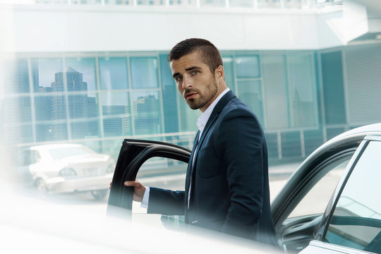 Handsome brutal man near the car, against theon the background of the business center. Luxury.