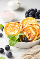 Cottage cheese fritters (syrniki) with fresh blueberries, mint and sauce. Light grey background. Healthy breakfast or diet lunch. Copy space.