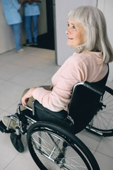 Smiling senior woman in wheelchair sitting at the hospital corridor. Go home after discharge from hospital