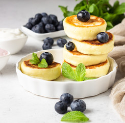 Cottage cheese fritters (syrniki) with fresh blueberries, mint and sauce. Light grey background. Healthy breakfast or diet lunch. Copy space.
