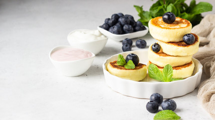 Cottage cheese fritters (syrniki) with fresh blueberries, mint and sauce. Light grey background. Healthy breakfast or diet lunch. Copy space.