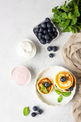 Cottage cheese fritters (syrniki) with fresh blueberries, mint and sauce. Light grey background. Healthy breakfast or diet lunch. Copy space.