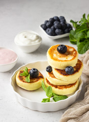 Cottage cheese fritters (syrniki) with fresh blueberries, mint and sauce. Light grey background. Healthy breakfast or diet lunch. Copy space.