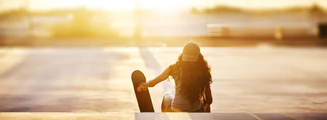 Fotobehang Rear view of young woman sitting with skateboard on steps at park during sunset panorama © Joshua Resnick