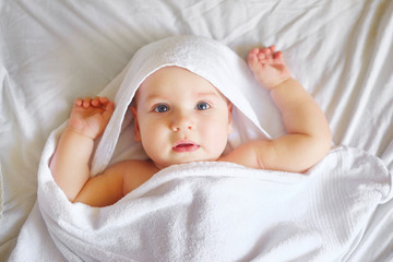 Fototapeta na wymiar Boy kid dressed in a white towel is lying on a white bed. Newborn baby is resting in bed after a bath or shower. Textiles and bedding for children.