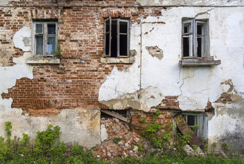 Fototapeta na wymiar The wall of the old house with Windows, requiring repair. Fallen off plaster. Brick wall