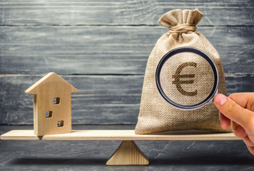 A money bag and a wooden house on the scales. The concept of real estate purchase. Sale of...