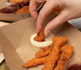 Mano mojando pollo frito en salsa blanca sobre mesa