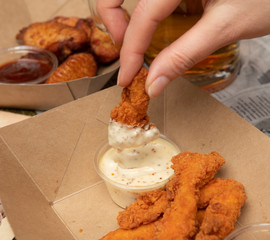 Mano mojando pollo frito en salsa blanca sobre mesa