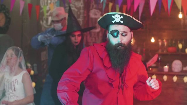 Handsome man dressed as a pirate is dancing at a halloween party. Captain hook with big black beard is having fun.