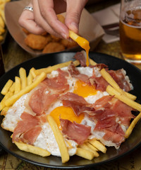 Mano con plato de huevos rotos con jamón, huevo frito, patatas y jamón