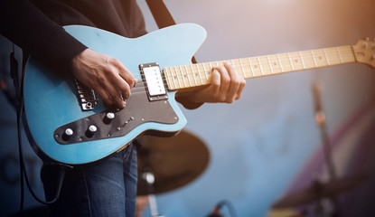 The guitarist performs a melody on a blue electric guitar, which is connected by a wire to the...