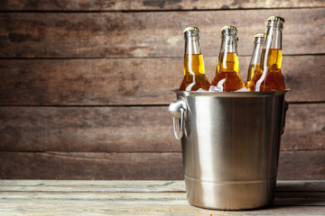 Cold bottles of beer in the bucket on the wooden background - obrazy, fototapety, plakaty