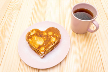 Heart shaped pancakes for romantic breakfast with strawberry jam and black tea. Shrovetide (carnival) concept. On wooden background