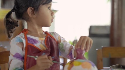 asian child painting ceramic pot with paint brush in pottery workshop