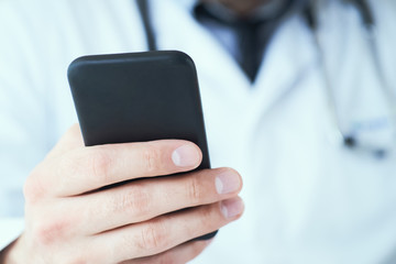 Male doctor hands with mobile phone close-up. Male doctor in white coat is using a modern smartphone device with touch screen.