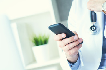 Male doctor in white coat is using a modern smartphone device with touch screen. Doctor hands with mobile phone.