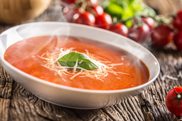 Hot tomato soup parmesan cheese and basil leave on old oal table