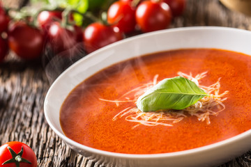 Hot tomato soup parmesan cheese and basil leave on old oal table