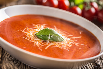 Hot tomato soup parmesan cheese and basil leave on old oal table