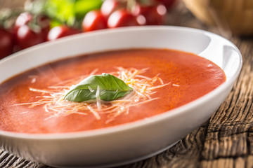 Hot tomato soup parmesan cheese and basil leave on old oal table