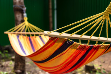 A multi-colored fabric hammock hangs in the trees, in the rays of the sun, in the open air.