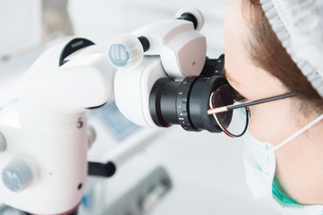 Close-up A woman in glasses with a professional dentist working with a professional stamotological microscope in her office. Stamotologist profession concept