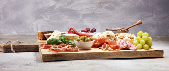 Cutting board with prosciutto, salami, cheese,bread and olives on dark stone background