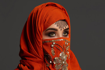 Studio shot of a young charming woman wearing the terracotta hijab decorated with sequins and jewelry. Arabic style.