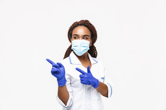 Image of brunette african american nurse or doctor woman wearing medical face mask and disposable gloves pointing fingers at copyspace