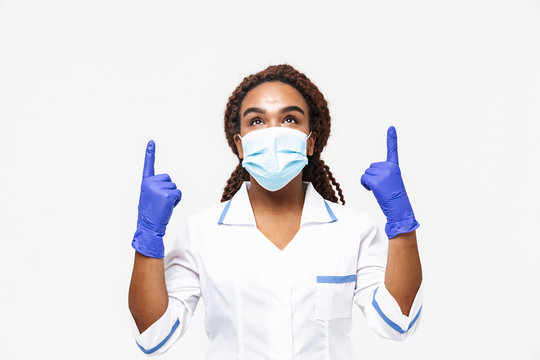 Image of happy african american nurse or doctor woman wearing medical face mask and disposable gloves pointing fingers at copyspace