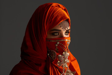 Studio shot of a young charming woman wearing the terracotta hijab decorated with sequins and jewelry. Arabic style.