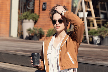 Fototapeta premium Young beautiful girl with a stylish haircut sits on the street and drinks coffee.