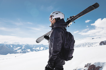 Fototapeta na wymiar Close-up Portrait bearded male skier aged against background of mountains. An adult man wearing ski googles mask and helmet skis on his shoulder looks mountains. Ski resort concept
