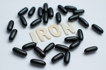 Iron medicament supplement. Black capsules with liquid inside. Inscription Iron by wooden letters. 