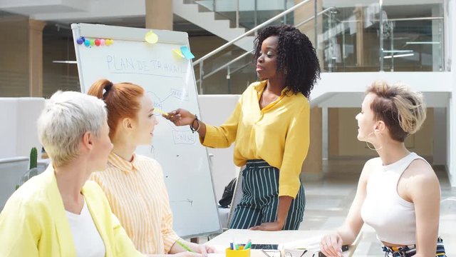 African stylish woman has orginized international woman's club. Afro girl pointing to the flipchart while explaining important information