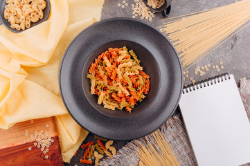 Different types of pasta on a black plate top view.