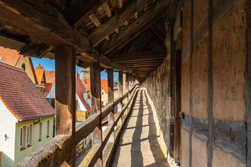 Fototapeta na wymiar Great view of the medieval wall-walk in the famous well preserved middle-age town Rothenburg ob der Tauber, Germany. The roofed defensive corridor with wooden railings offers a nice view to the town.