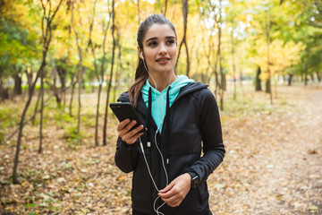 Young pretty fitness woman outdoors in the park using mobile phone.